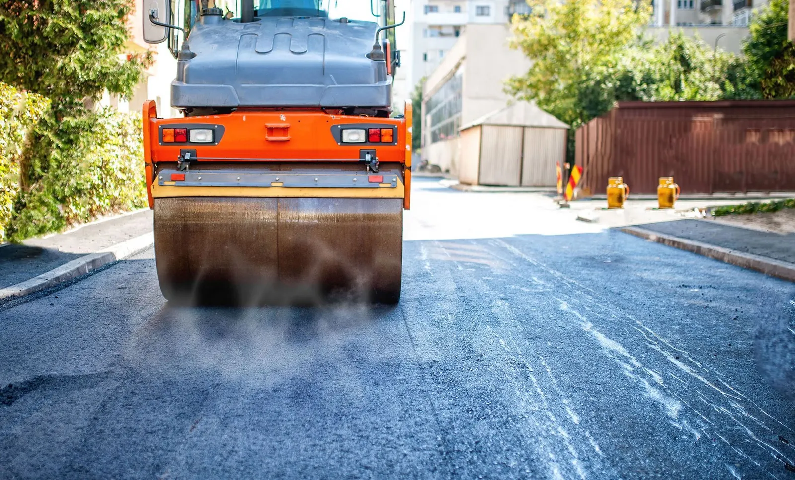 Freshly paved black asphalt driveway leading to a two-story brick home surrounded by trees.